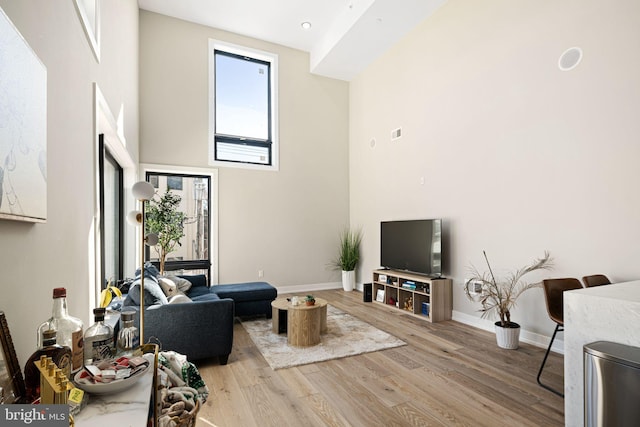 living area featuring visible vents, a high ceiling, baseboards, and wood finished floors