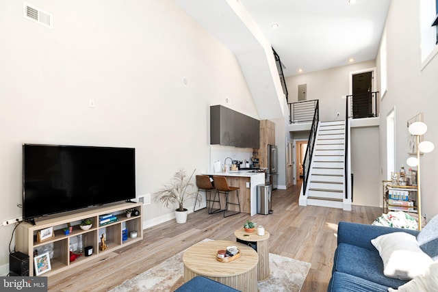 living room with visible vents, baseboards, stairway, a high ceiling, and light wood-style floors