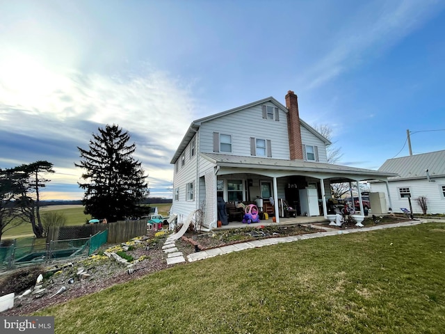 rear view of property featuring a chimney, fence, a yard, and covered porch