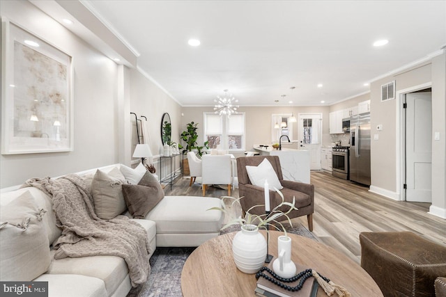 living area with crown molding, a notable chandelier, visible vents, and light wood finished floors