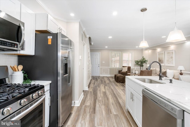 kitchen featuring light wood-style flooring, a sink, stainless steel appliances, crown molding, and open floor plan