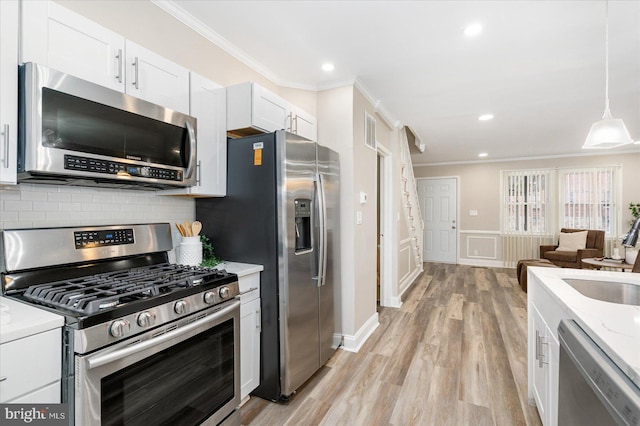 kitchen with tasteful backsplash, ornamental molding, light wood-style floors, white cabinets, and stainless steel appliances