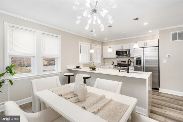 kitchen featuring light wood finished floors, crown molding, light countertops, appliances with stainless steel finishes, and a sink