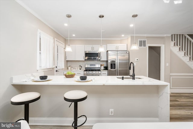 kitchen with a sink, backsplash, wood finished floors, appliances with stainless steel finishes, and a breakfast bar area