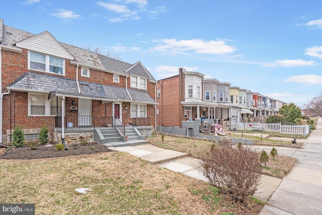 townhome / multi-family property featuring brick siding, fence, a residential view, a high end roof, and a front yard