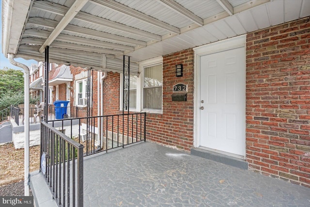 view of exterior entry with brick siding and a porch