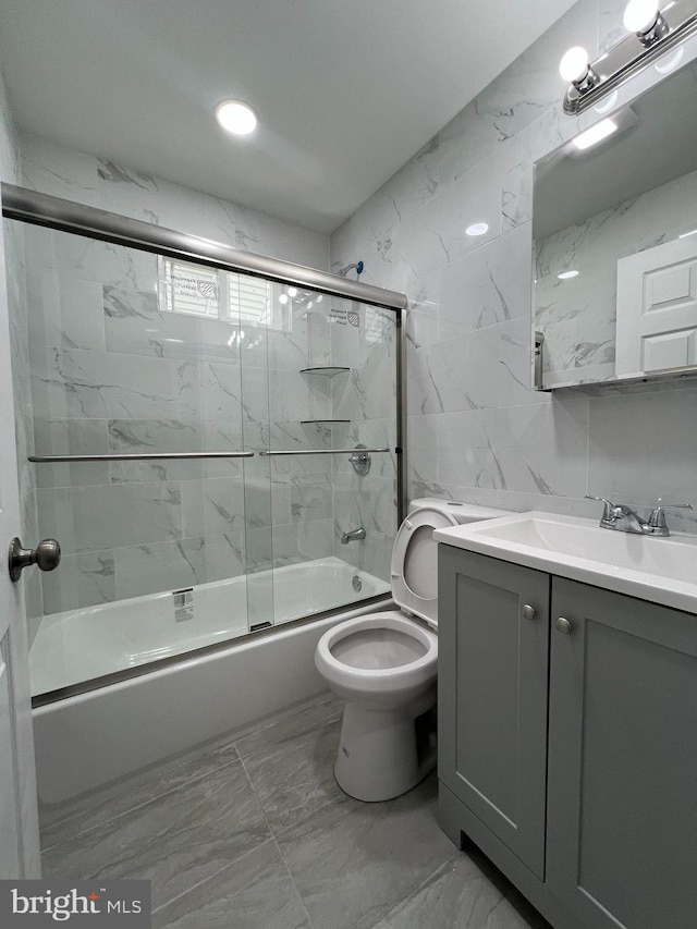 bathroom with toilet, marble finish floor, tile walls, enclosed tub / shower combo, and vanity