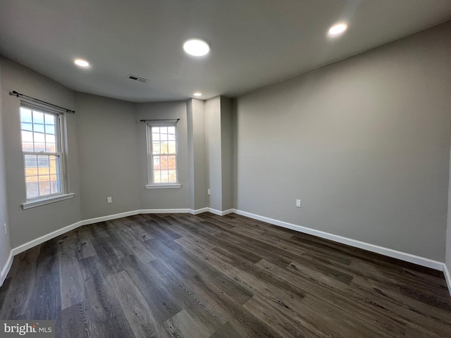 spare room with a wealth of natural light, visible vents, baseboards, and dark wood-type flooring