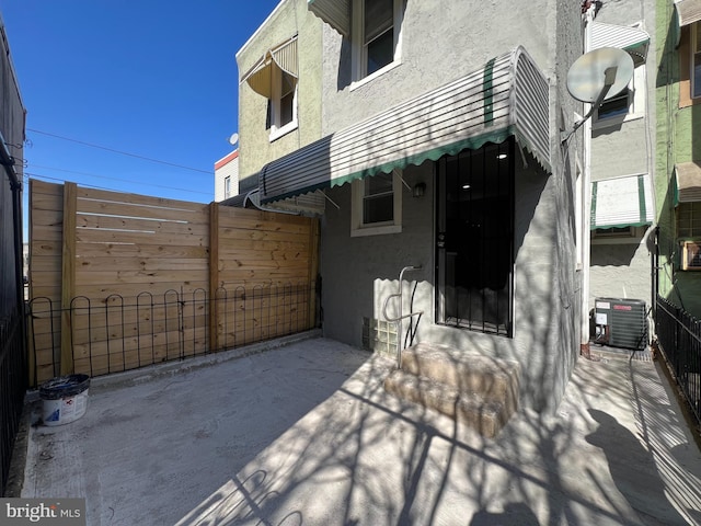 back of house featuring central AC unit, stucco siding, and fence