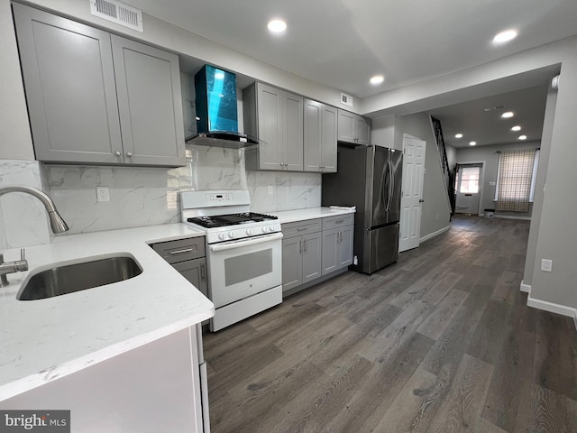 kitchen with gray cabinets, freestanding refrigerator, a sink, white gas range oven, and wall chimney exhaust hood