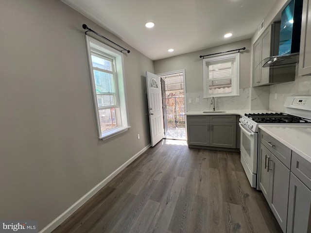 kitchen featuring gray cabinetry, a sink, backsplash, wall chimney range hood, and white gas range