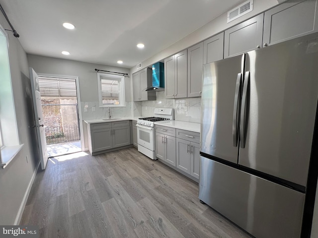 kitchen with white range with gas cooktop, gray cabinets, freestanding refrigerator, a sink, and wall chimney exhaust hood