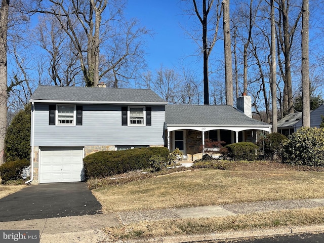 split level home featuring roof with shingles, a porch, an attached garage, a chimney, and aphalt driveway