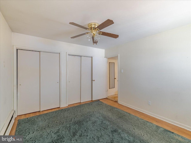 unfurnished bedroom featuring baseboards, ceiling fan, multiple closets, wood finished floors, and a baseboard radiator