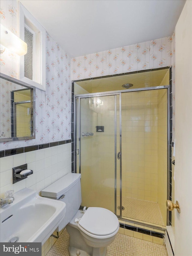 bathroom with a stall shower, a sink, tile walls, wainscoting, and wallpapered walls