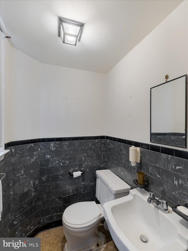 bathroom with a wainscoted wall, toilet, tile walls, and a sink