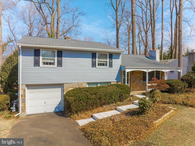 split level home featuring stone siding, driveway, a chimney, and an attached garage