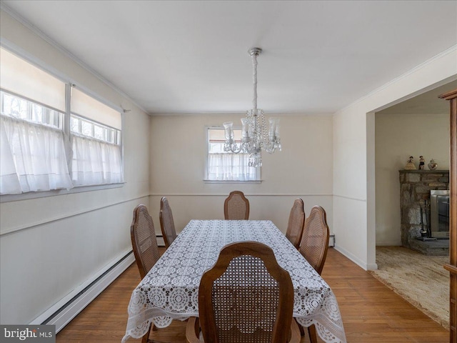 dining space featuring a baseboard radiator, an inviting chandelier, wood finished floors, and crown molding