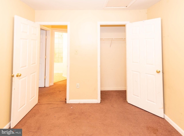 unfurnished bedroom with a closet, light carpet, baseboards, and attic access