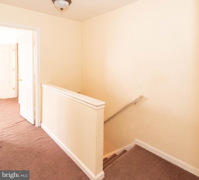 hallway featuring an upstairs landing, baseboards, and carpet floors