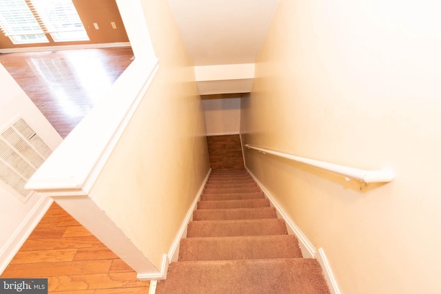 staircase with wood finished floors, visible vents, and baseboards