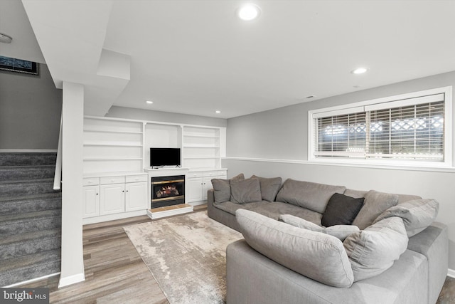 living area with visible vents, a glass covered fireplace, recessed lighting, stairway, and light wood-style floors