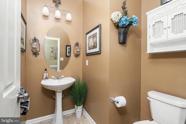 half bath with tile patterned floors, toilet, and baseboards