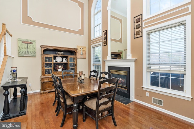 dining area featuring visible vents, baseboards, a fireplace with flush hearth, a towering ceiling, and wood finished floors