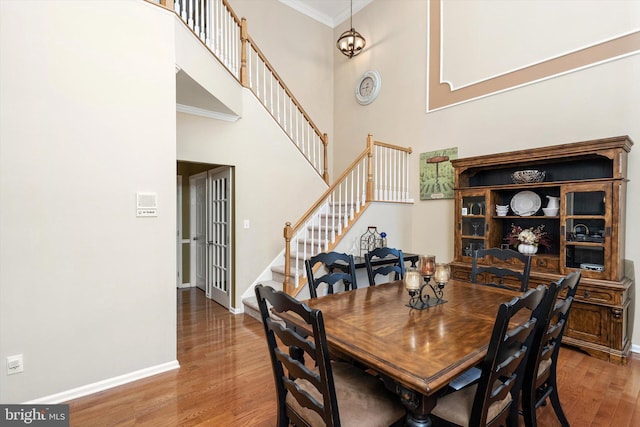 dining room featuring wood finished floors, stairway, a high ceiling, crown molding, and baseboards