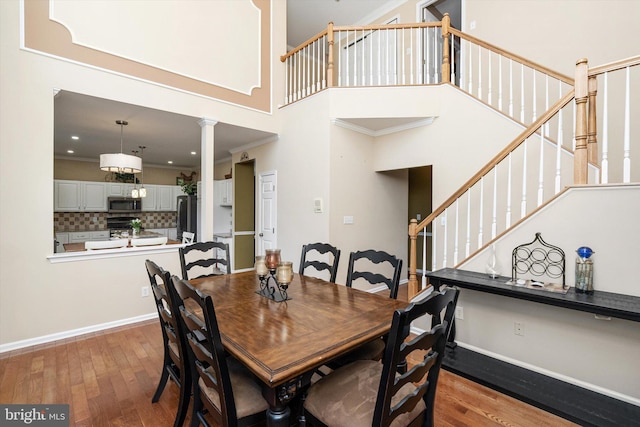 dining area with wood finished floors, baseboards, stairs, a towering ceiling, and crown molding