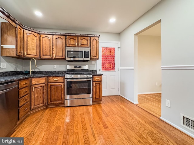 kitchen with light wood finished floors, visible vents, brown cabinetry, stainless steel appliances, and a sink