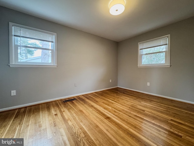 unfurnished room featuring a wealth of natural light, visible vents, baseboards, and wood finished floors