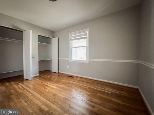 unfurnished bedroom featuring visible vents, two closets, baseboards, and wood finished floors