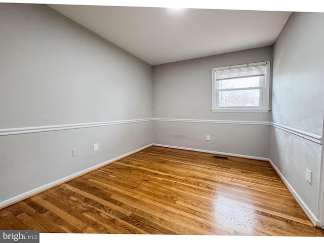 spare room with wood finished floors, visible vents, and baseboards