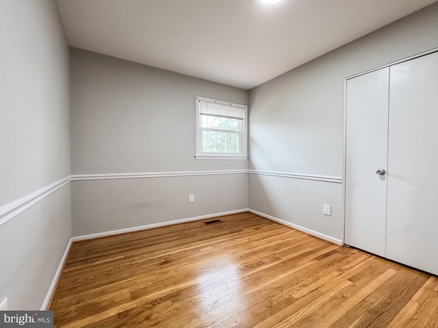 unfurnished bedroom featuring wood finished floors, visible vents, a closet, and baseboards