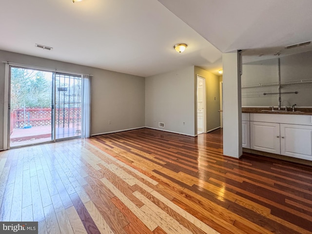 unfurnished living room featuring visible vents, wood-type flooring, baseboards, and a sink