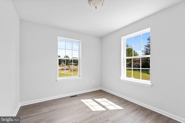 empty room with visible vents, a healthy amount of sunlight, and wood finished floors