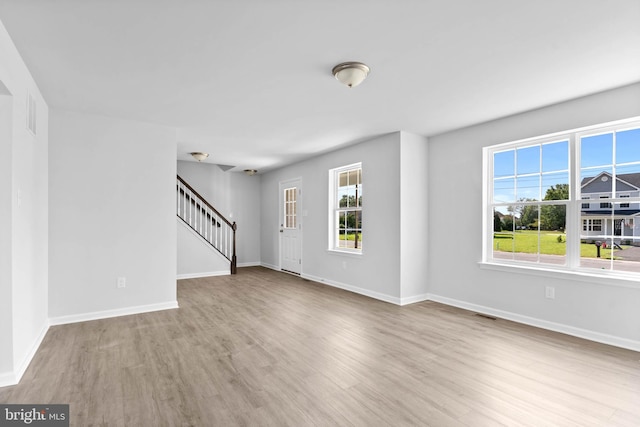 unfurnished living room with a wealth of natural light, stairway, baseboards, and wood finished floors