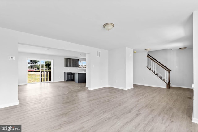 unfurnished living room with stairs, visible vents, baseboards, and light wood-type flooring