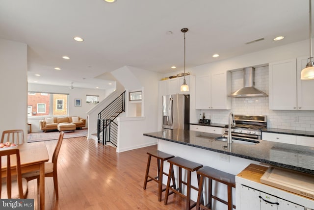 kitchen with light wood finished floors, a sink, appliances with stainless steel finishes, wall chimney range hood, and tasteful backsplash