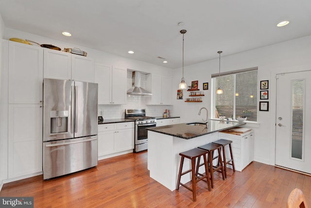 kitchen with a kitchen breakfast bar, wood finished floors, stainless steel appliances, wall chimney exhaust hood, and a sink