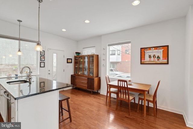 kitchen with a breakfast bar, a sink, dark stone countertops, wood finished floors, and recessed lighting