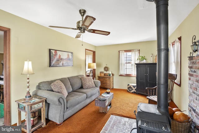 living room featuring a wood stove, a ceiling fan, and carpet floors