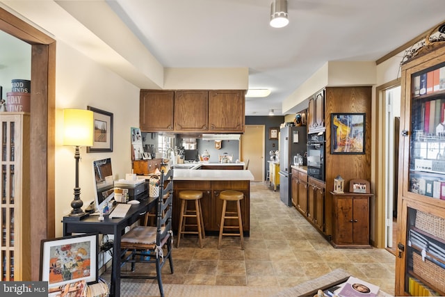 kitchen featuring oven, a breakfast bar area, light countertops, a peninsula, and freestanding refrigerator