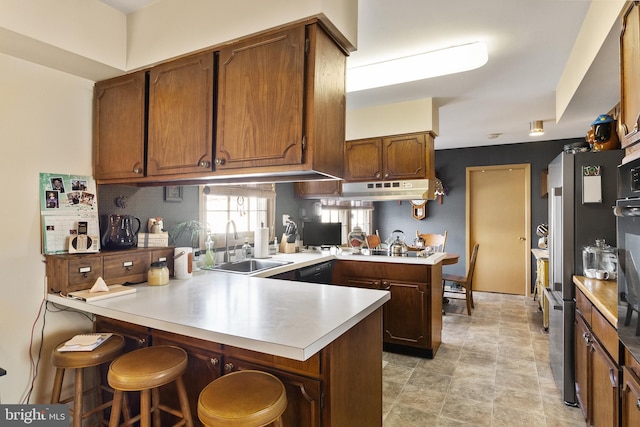 kitchen with a peninsula, light countertops, under cabinet range hood, and a sink