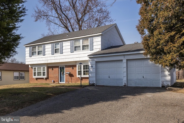 colonial home featuring a front yard, driveway, an attached garage, a shingled roof, and brick siding