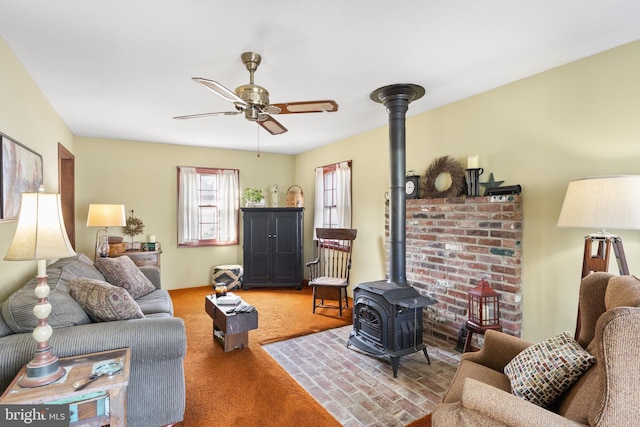 carpeted living area with a wood stove and ceiling fan