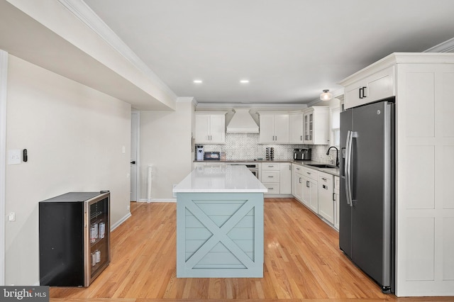 kitchen featuring tasteful backsplash, custom exhaust hood, stainless steel fridge, white cabinetry, and a sink