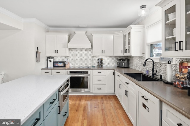 kitchen with a sink, premium range hood, white cabinetry, and oven