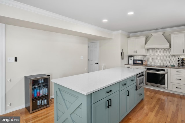 kitchen featuring custom range hood, light wood-style flooring, white cabinets, and oven